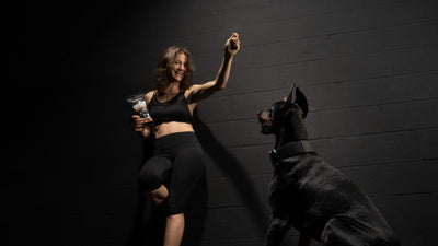 Woman holding up a training treat for her sitting Doberman against a black brick wall